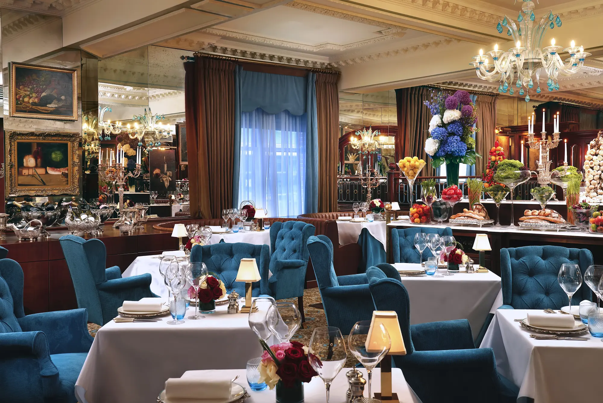 a fancy dining room with square tables covered with white tablecloths and surrounded by blue chairs