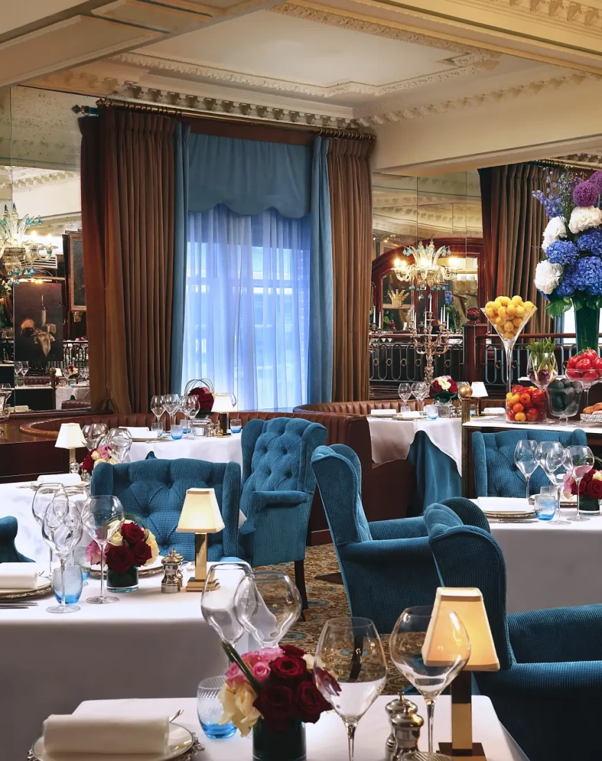 a fancy dining room with square tables covered with white tablecloths and surrounded by blue chairs