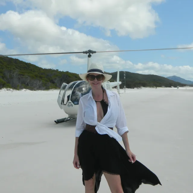 Travel advisor Nandi Shenkan in black and white dress standing in front of a helicopter.