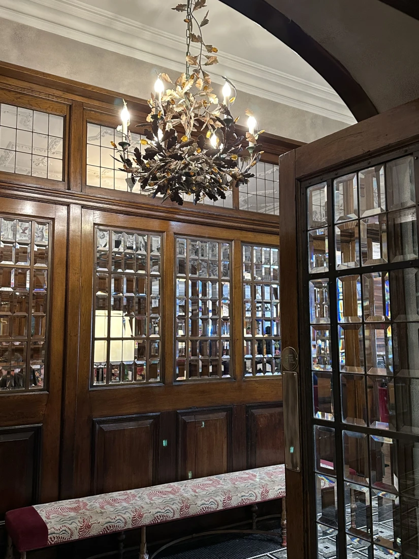 The foyer of Brown's Hotel with wood paneled doors and glass windows divided into small squares and a chandelier