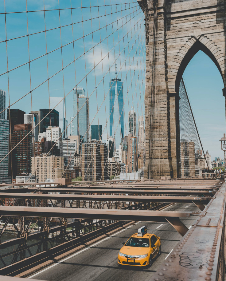 yellow taxi driving over large bridge with city skyline in the background