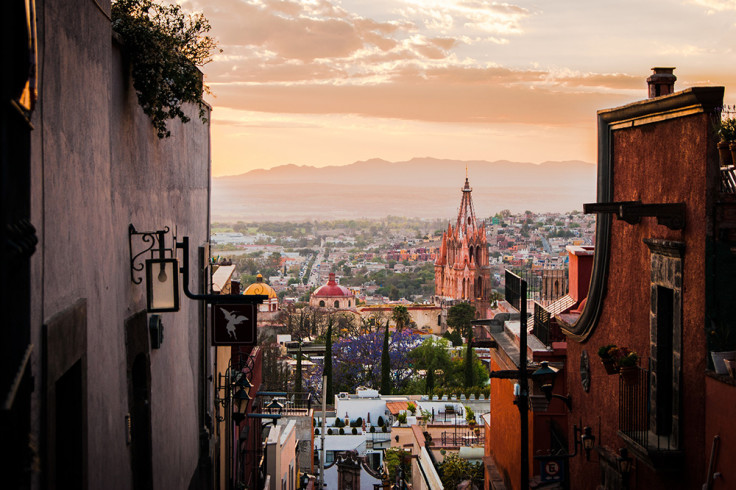 San Miguel de Allende Mexico view of the city at sunset with pink clouds and mountains in the background framed with red and white walls and metal light fixtures
