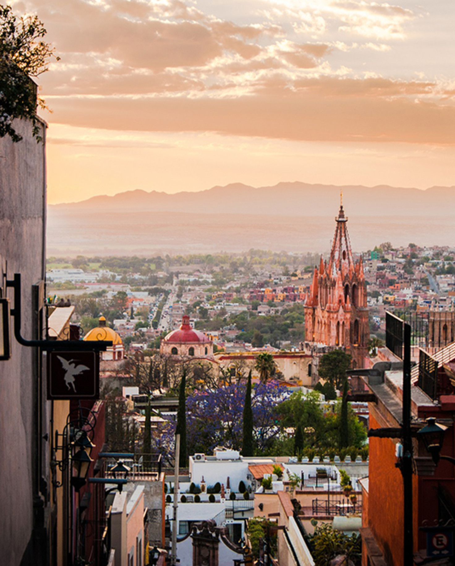 San Miguel de Allende Mexico view of the city at sunset with pink clouds and mountains in the background framed with red and white walls and metal light fixtures