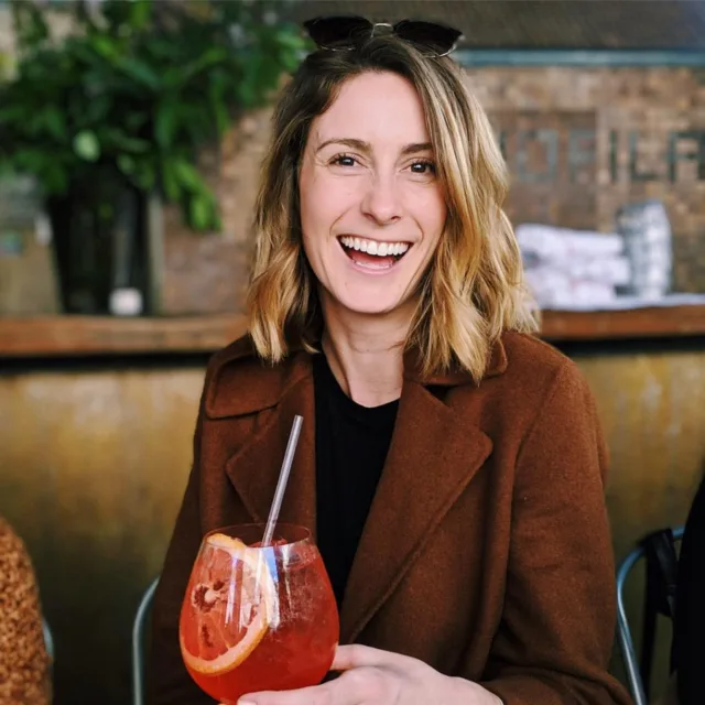 Fora travel agent Rachel Meyers wearing brown jacket holding a drink with grapefruit