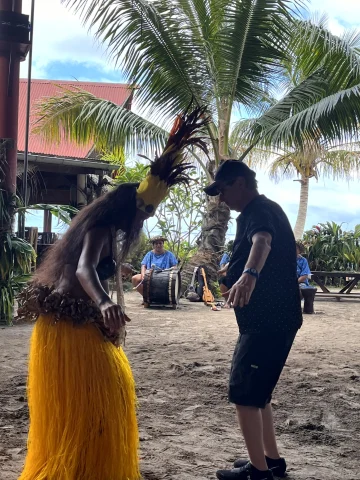 A traditional dancer teaching how to dance to a man on a beach.