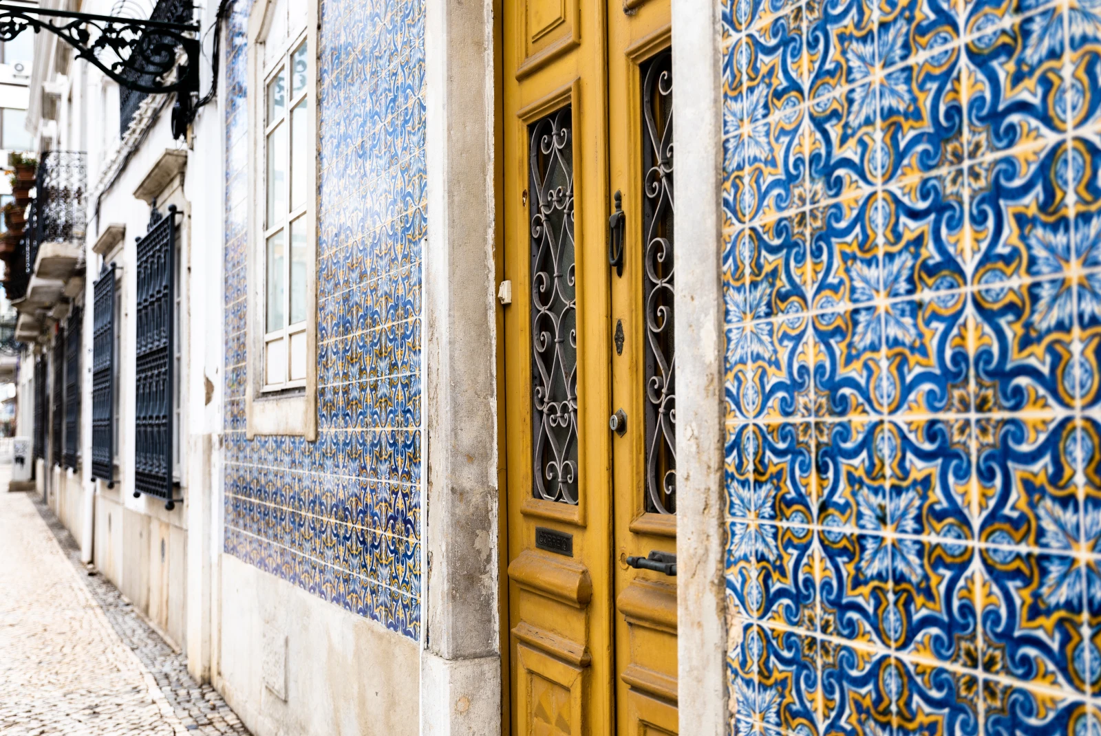 Building with blue and yellow tile wall and burnt yellow door in Portugal