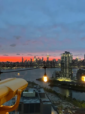 A view of the Manhattan skyline at sunset next to observation binoculars.