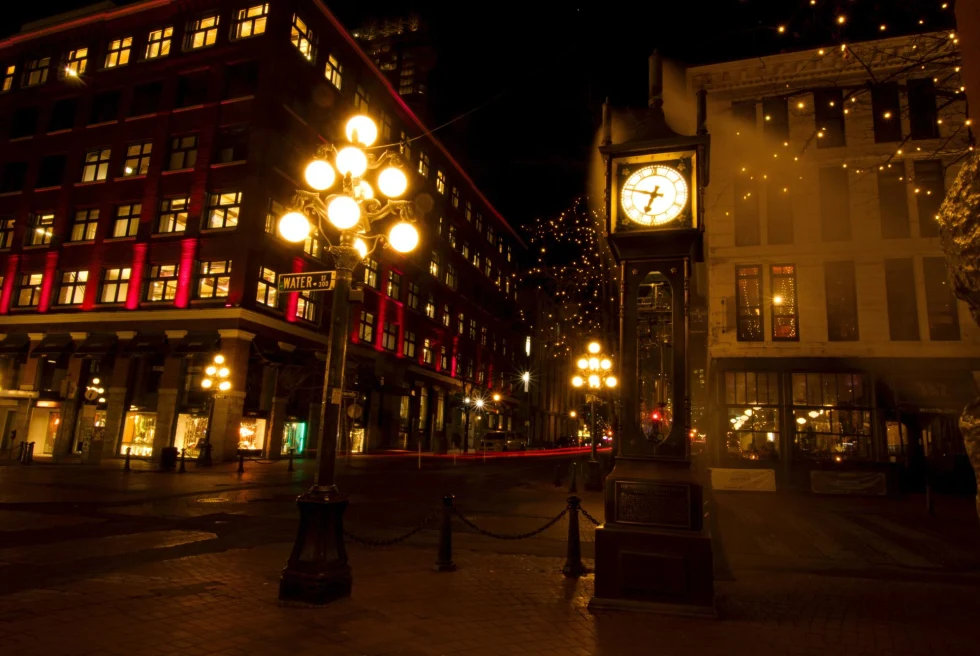 intersection of a quiet city street at night lit by lamplight and a small analog clock tower