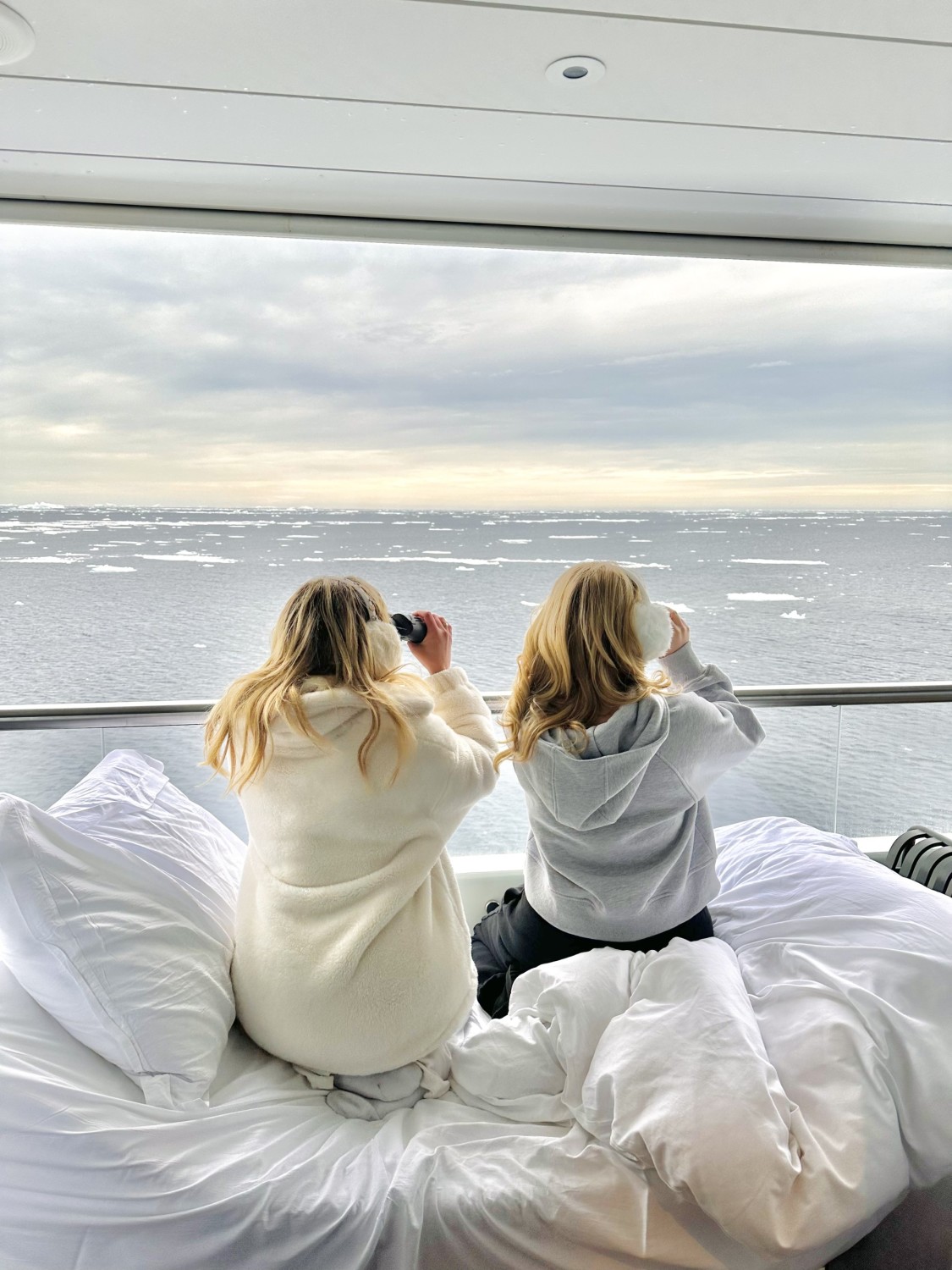 Two people sitting on a bed looking out of a cruise ship window to the sea