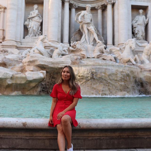 Fora travel agent Mary Xiao wearing red dress sitting at fountain in Italy