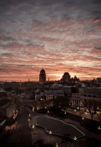 A view of a sunset and rippling clouds over Quebec City with street lamps and trees in the forefront. 