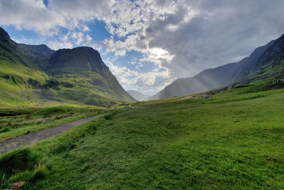 lush green fields amidst mountains with sunlight pouring through