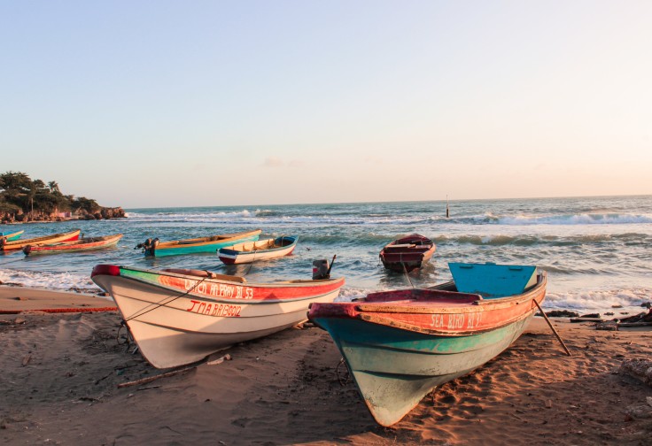 two white red and blue boats on a tan sandly beach at sunset with pink skies and blue ocean water with white crashing waves