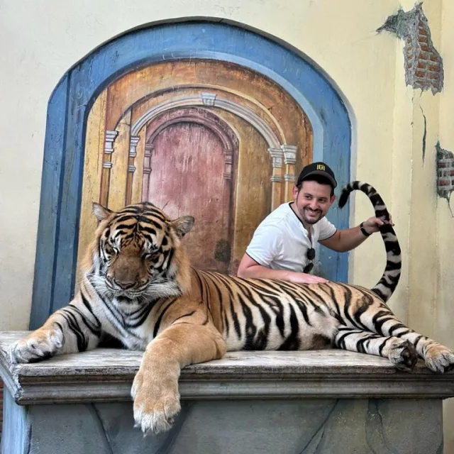 Picture of Mike wearing a white t-shirt and posing with a tiger laying down in front of him