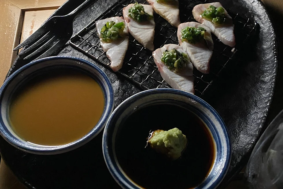 plate filled with sashimi, accompanied by two bowls of sauce