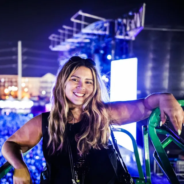 Travel Advisor Marie Roussel in a black shirt standing in front of a concert with purple lights.