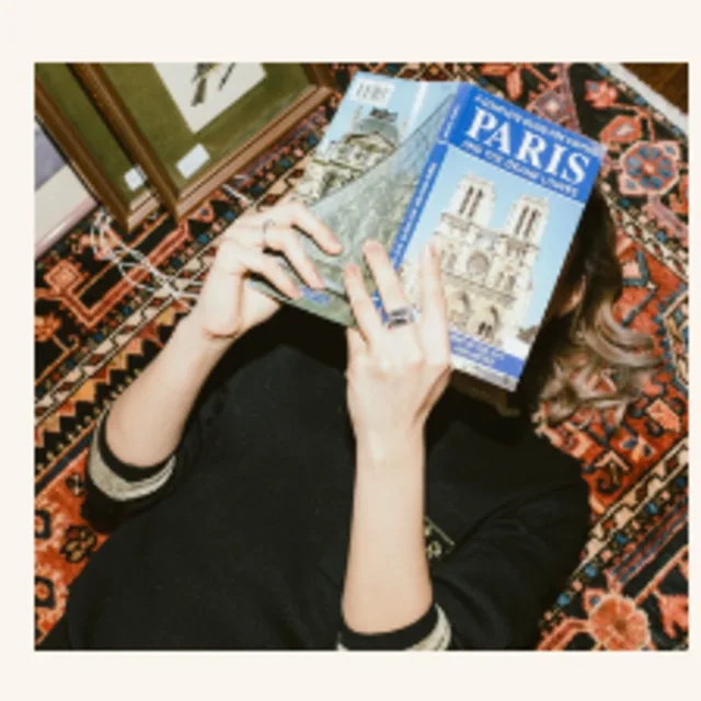 Travel advisor Ellie Geller reading a book named PARIS keeping close to her face.