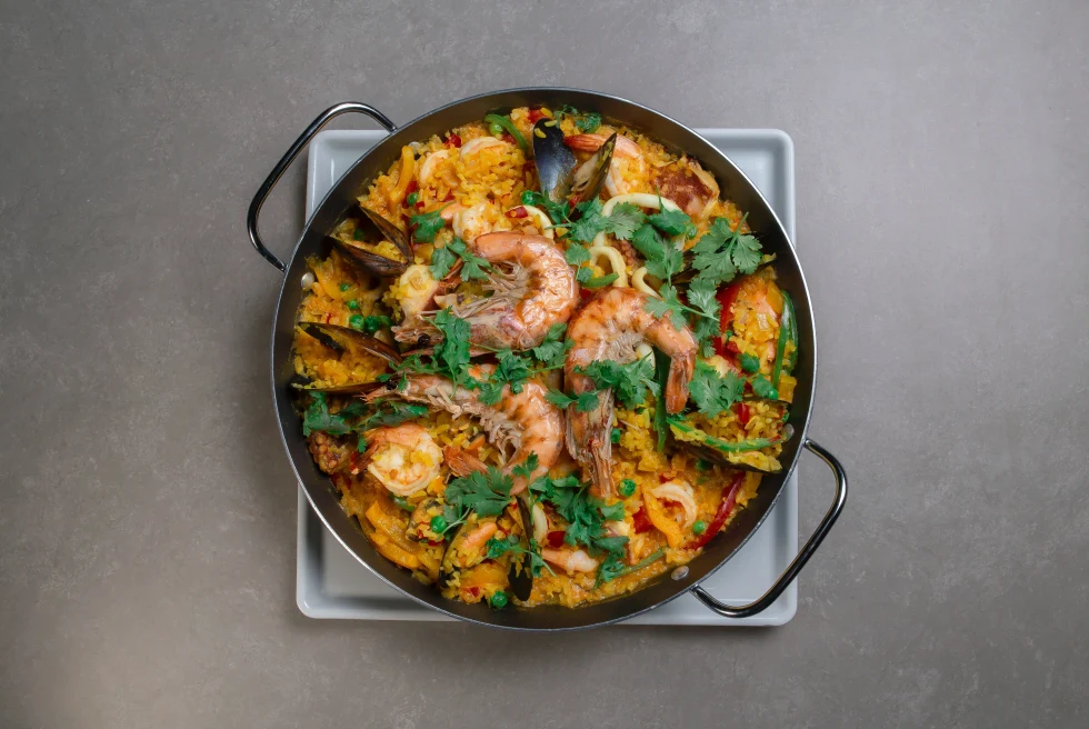 paella on a gray table with yellow rice and seafood and green parsley