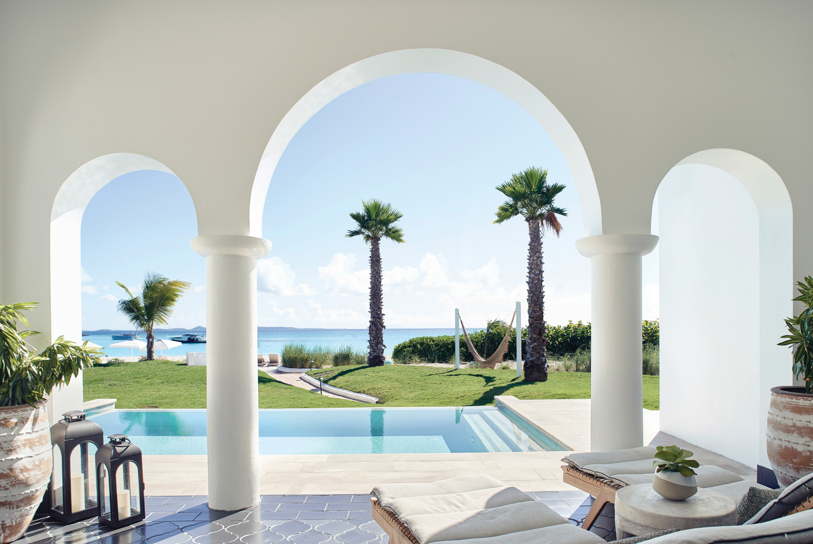 lounge chairs next to pool and palm trees overlooking the ocean