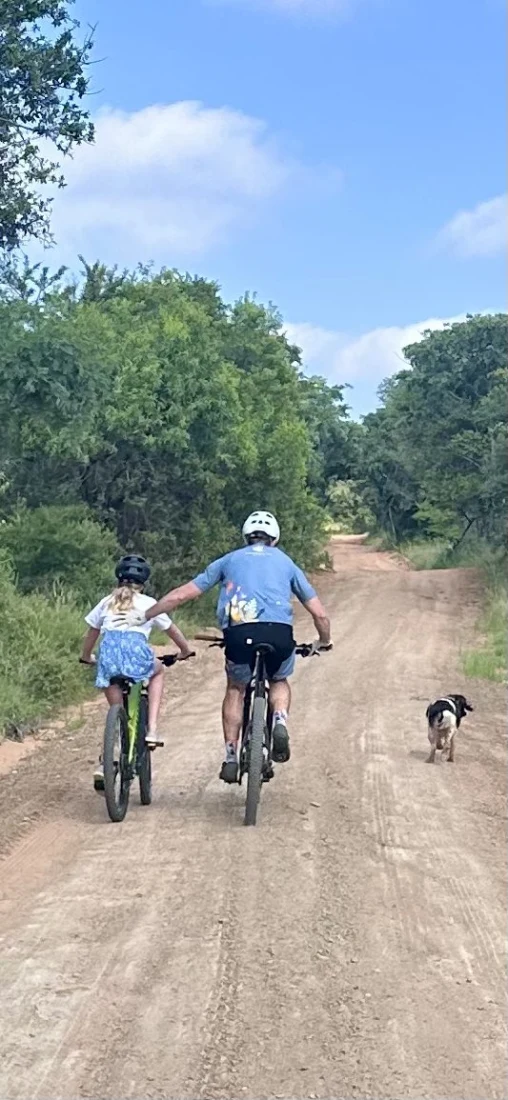 A dirt bike trail with two people and an animal traveling forward. They are also surrounded by trees on each side. 