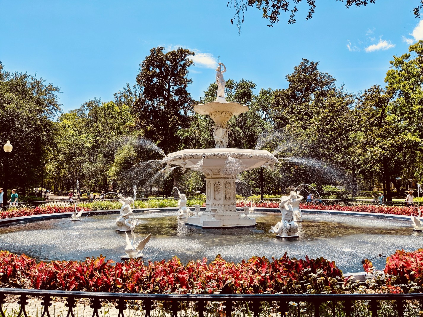 White fountain surrounded by red bushes and green trees on a sunny day in Georgia