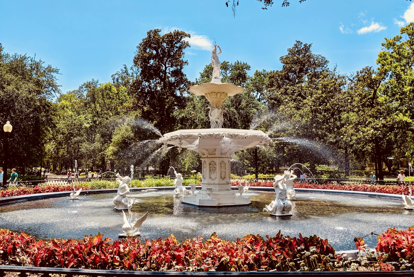 White fountain surrounded by red bushes and green trees on a sunny day in Georgia