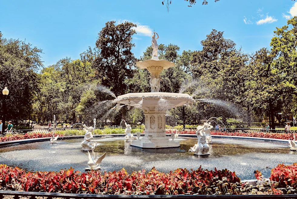 White fountain surrounded by red bushes and green trees on a sunny day in Georgia