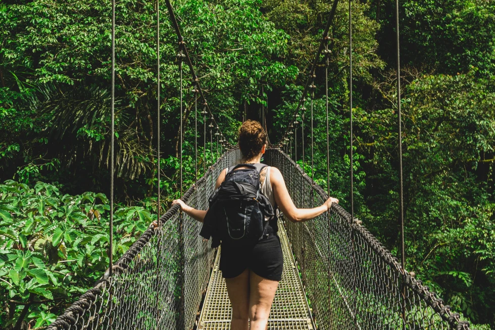 Girls walking on a bridge having a backpack in between a jungle