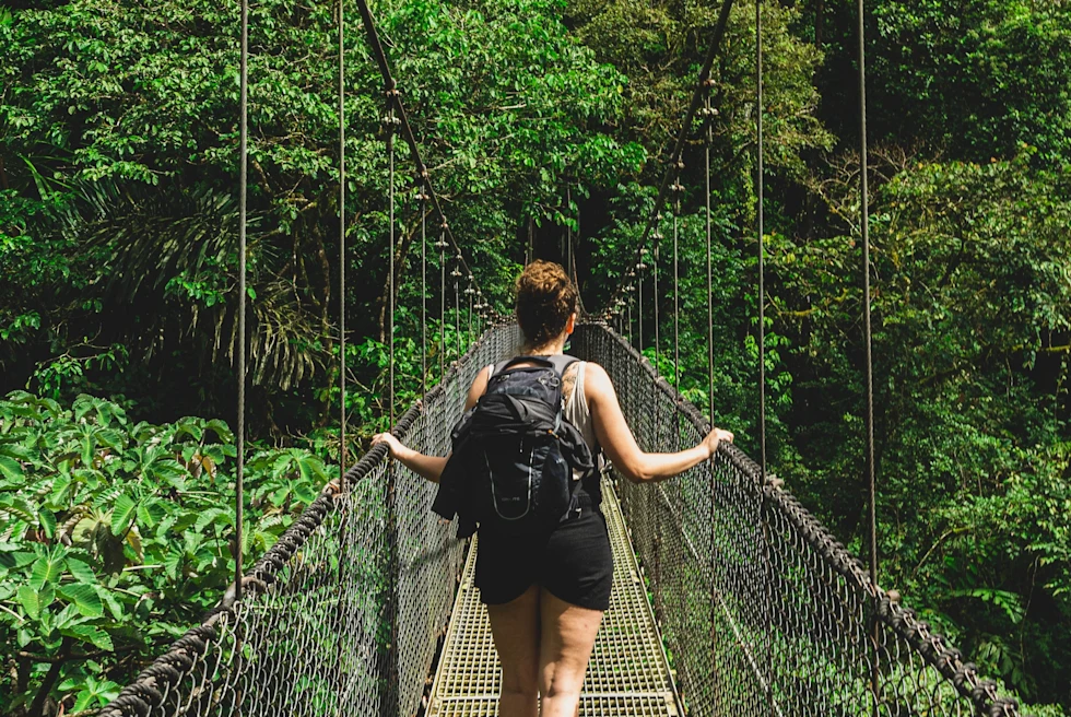 Girls walking on a bridge having a backpack in between a jungle