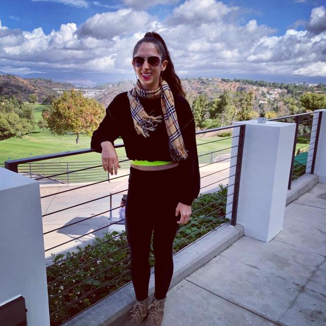 Fora travel agent wearing white pants and shirt standing next to railing with white clouds in the sky