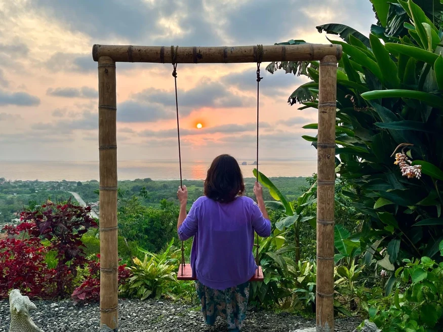 woman on a swing with her back turned watching the sunset over the jungle