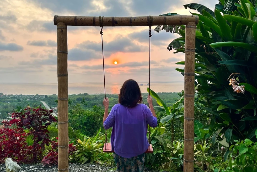 woman on a swing with her back turned watching the sunset over the jungle