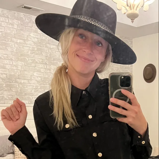Travel Advisor Mackenzie Williams with a black hat and shirt taking a mirror selfie.