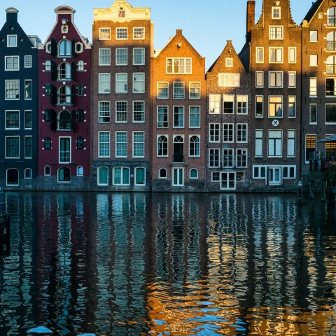 multiple story houses with big white windows on a canal reflect into the water below on a clear day