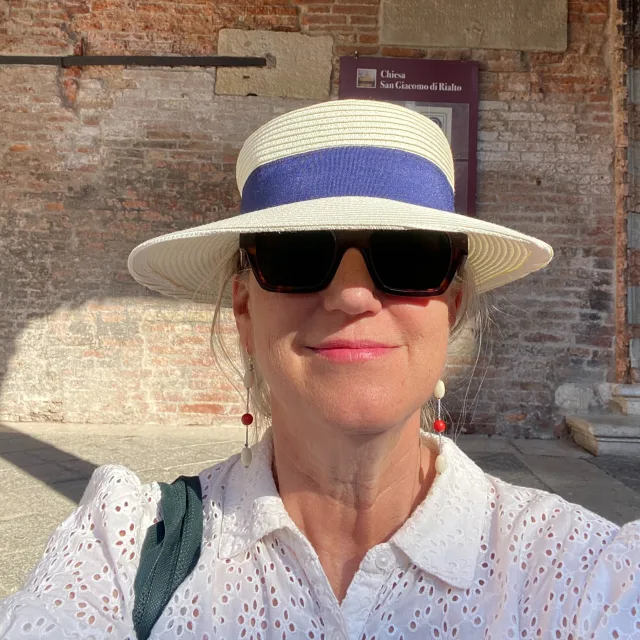 Travel Advisor Lauren Brown in a purple and tan hat and white shirt in front of a brick wall.
