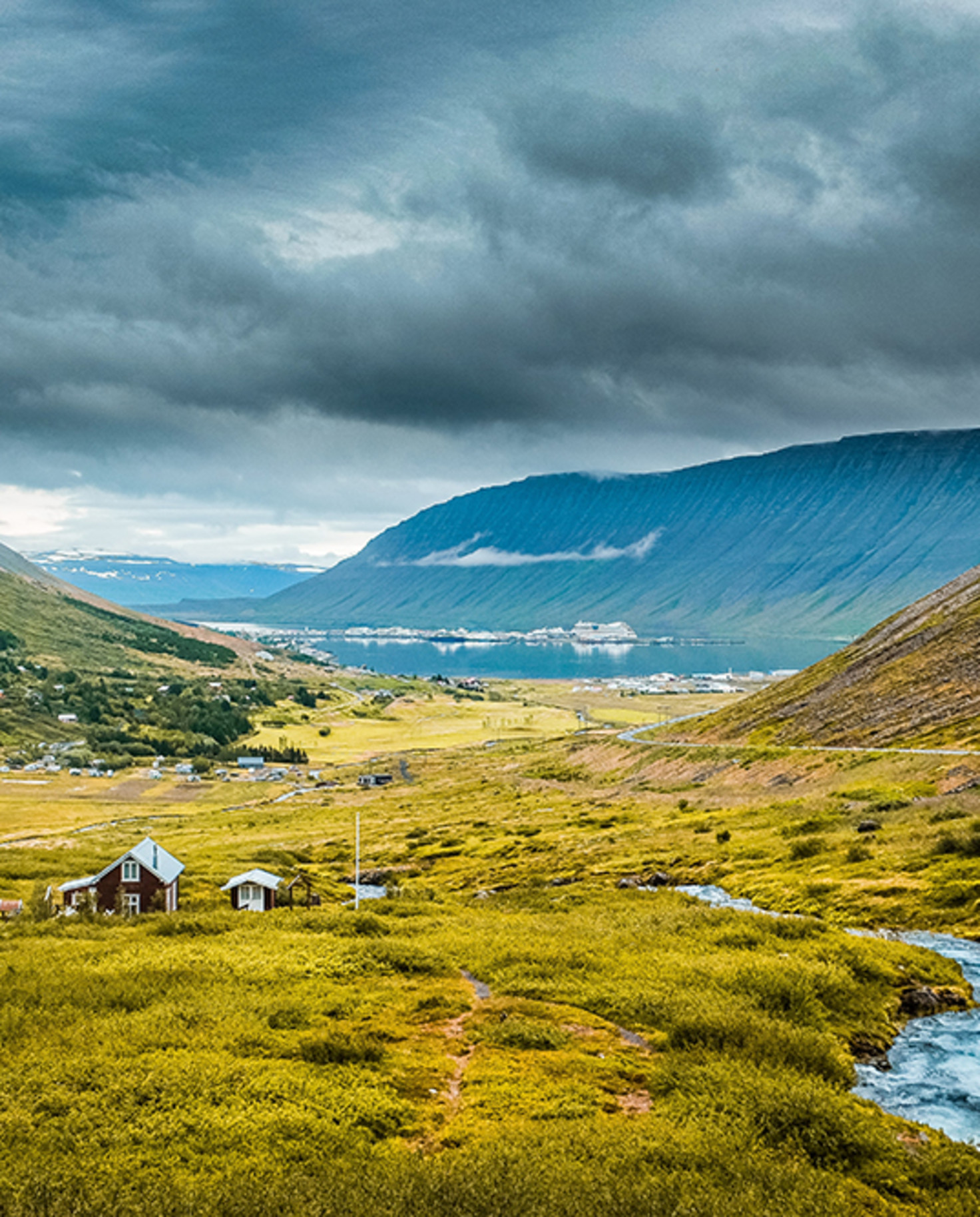 A skyline view of mountains in the Westfjords, Iceland with small houses in the central valley.