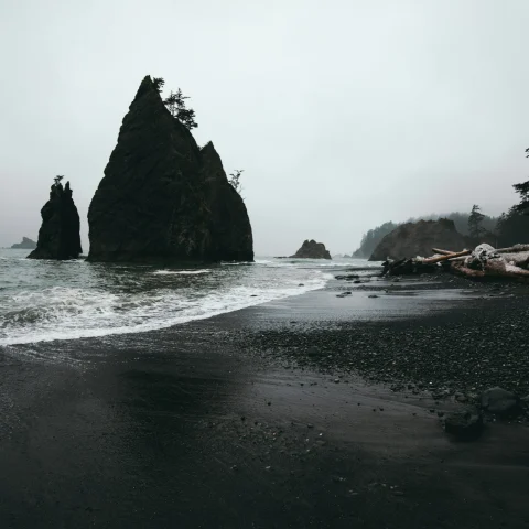 Black sand beach on a cloudy day with rock formations in the water