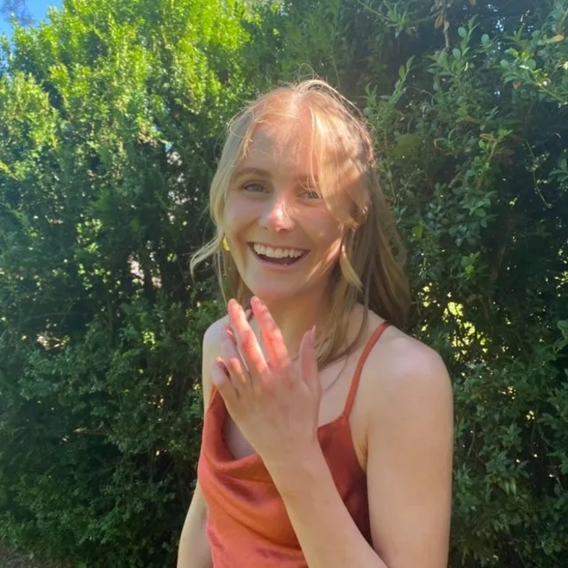 Travel Advisor Emma Wetenhall in orange dress in front of green shrubs.