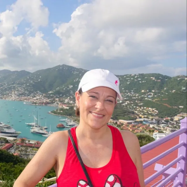 Travel advisor Monika Morris sitting on a bridge in red sleeveless shirt and a valley in the background.