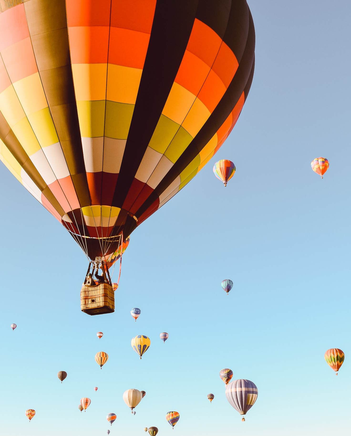 Red, yellow, white, orange, and black hot air balloon floats in the sky with other hot air balloons in the background in a clear blue sky