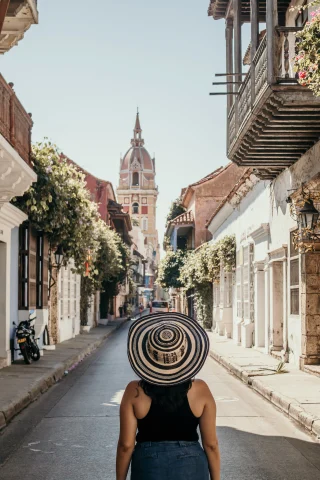 A person wearing a patterned hat standing in a street with their back to the camera during daytime