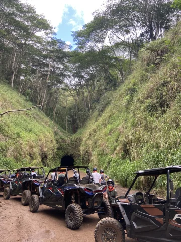 A row of black jeeps in a hilly area near tunnel. 