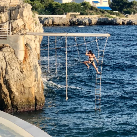 DuCapTrapeze - a woman in a black swimsuit on a ropes course over the sea that is attached to a rocky cliffside