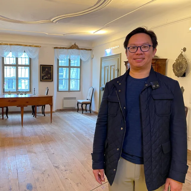 Travel Advisor Jason Cheng in a black and blue jacket in an antique filled room.