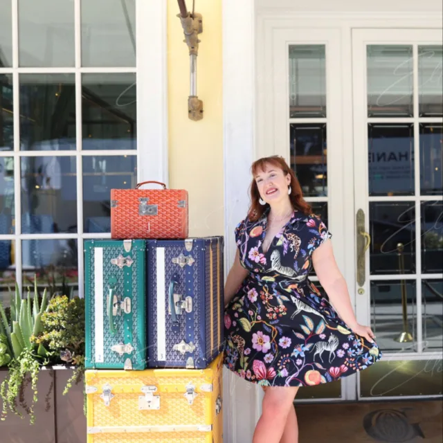 Leah Winstead in a blue floral print dress standing next to stacked luggage 