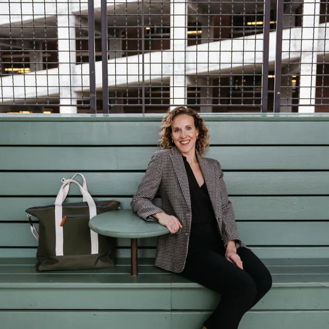 woman wearing black pants and blazer sitting on green bench