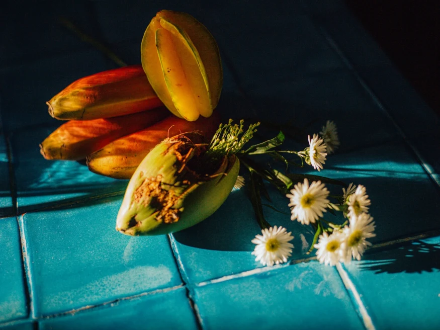 tropical fruits and daisies lying on a blue-tiled countertop
