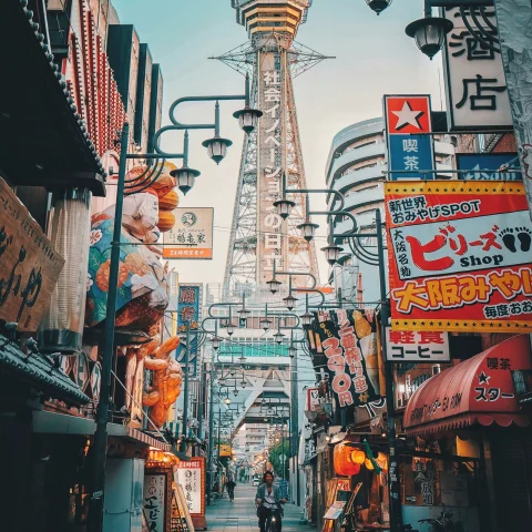 A low-angled view of a city street with colorful billboards and a tower in the distance