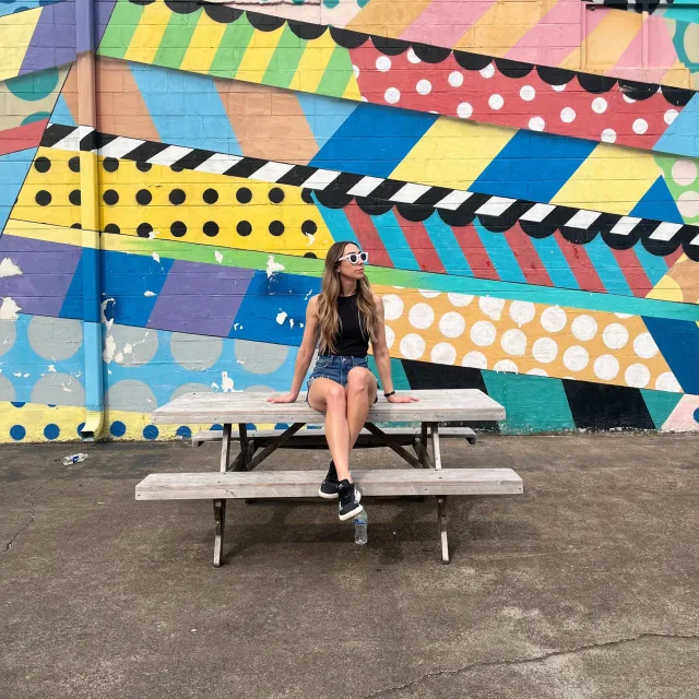 Travel Advisor Alyssa Poe is sitting on a bench in front of a colorful painted wall.
