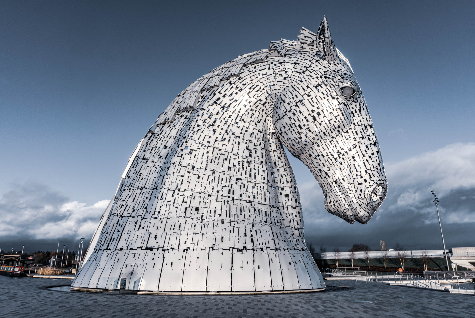 A giant white and silver horse head statue with a dark sky and black stone called the Kelpies in Scotland.